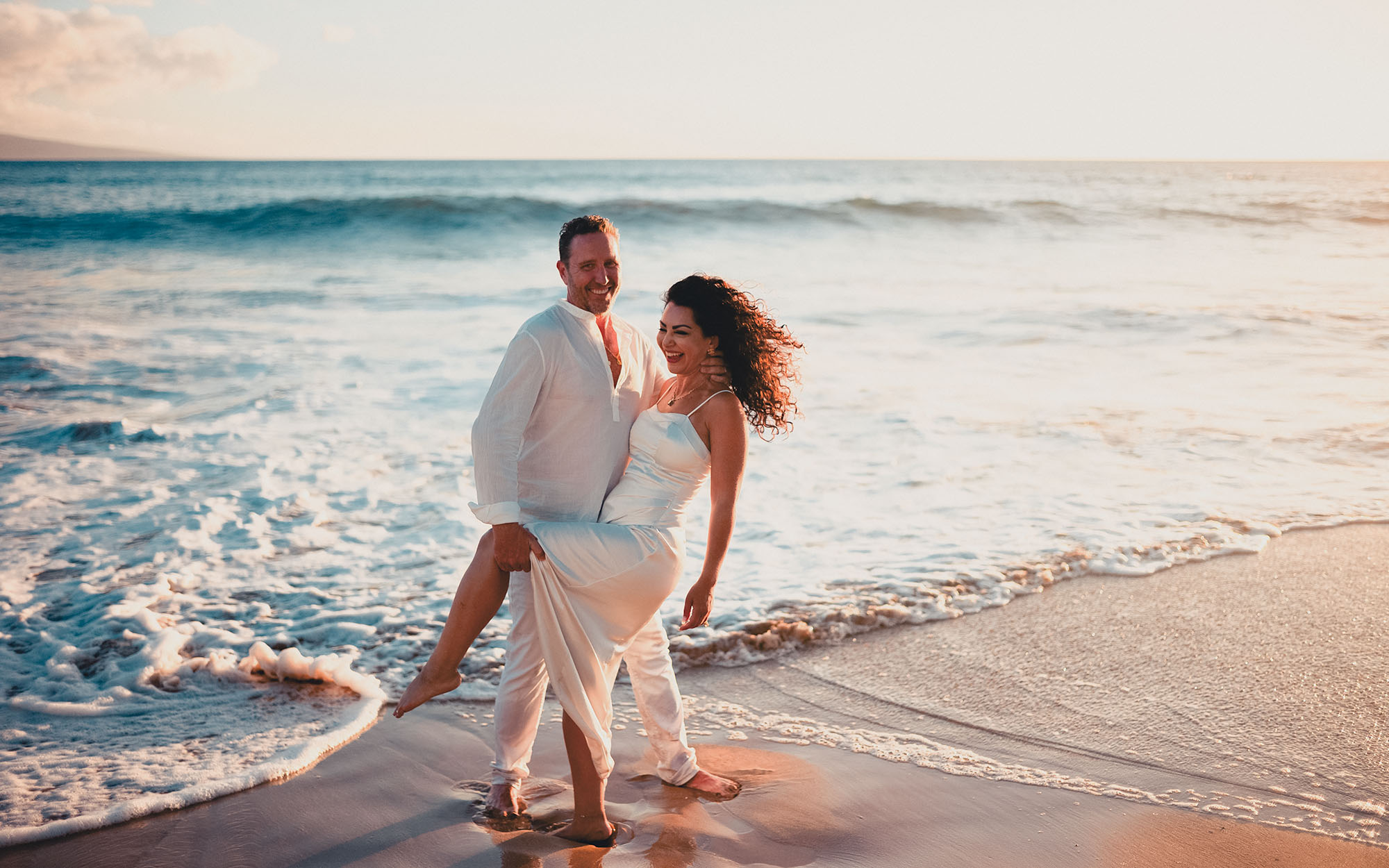 A couple walking together through the shallows at sunset on a Maui beach - image by Wailea Photo®