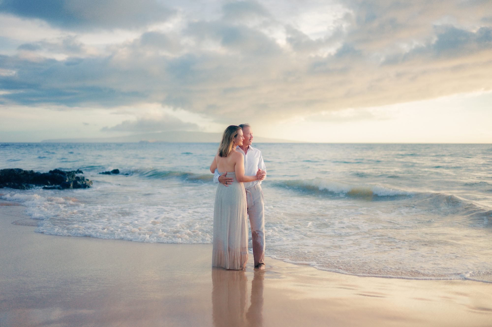 An engaged couple embracing at sunset on a Wailea beach
