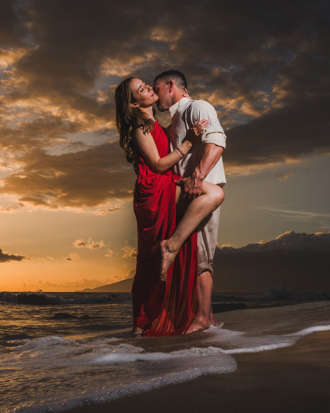 Couple embracing on the shoreline at dramatic golden-hour sunset in Wailea