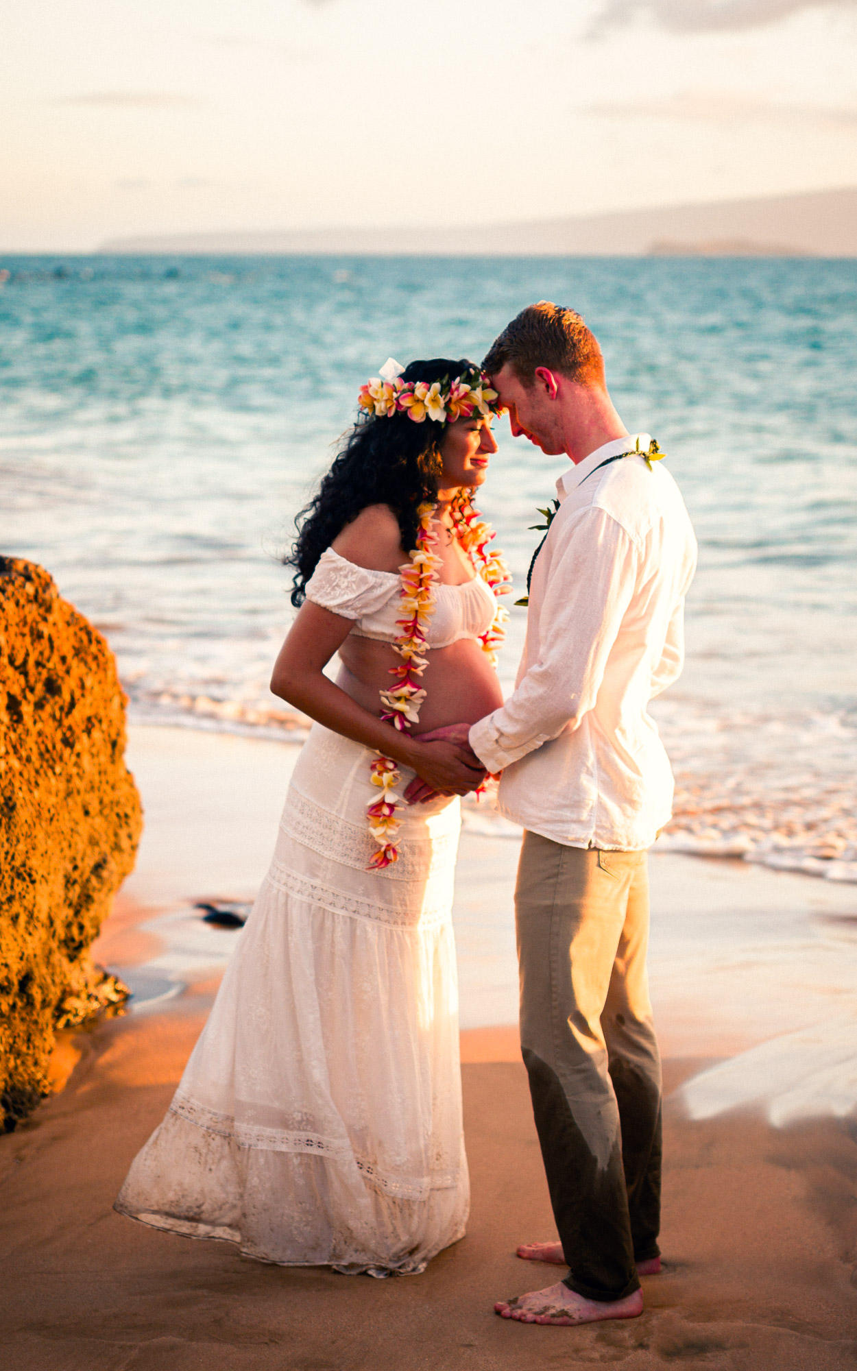 Couple in lei standing forehead to forehead beside lava rock at sunset in Maui - image by Wailea Photo®