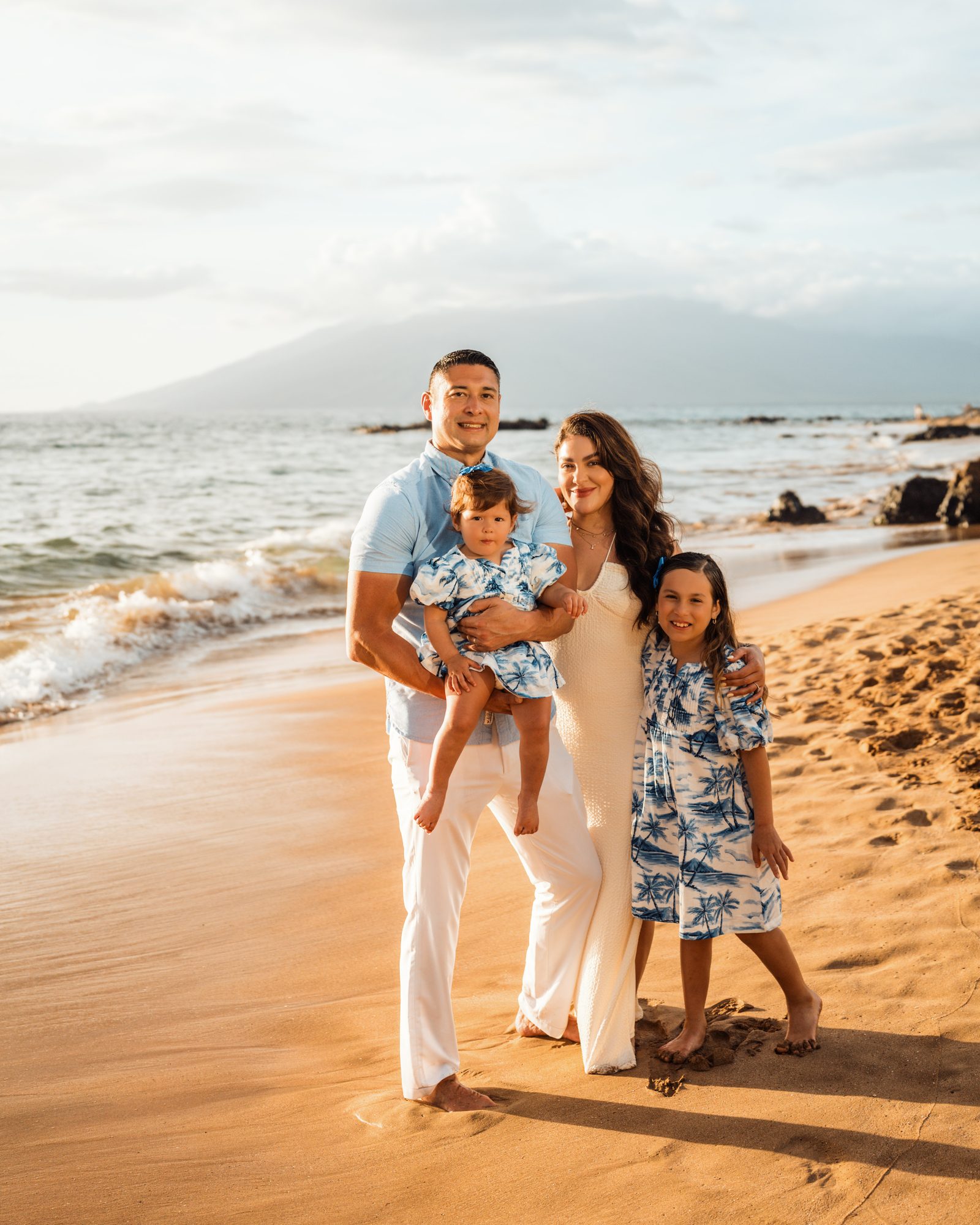 A family in coordinated blue and white outfits on a Wailea beach in soft morning light
