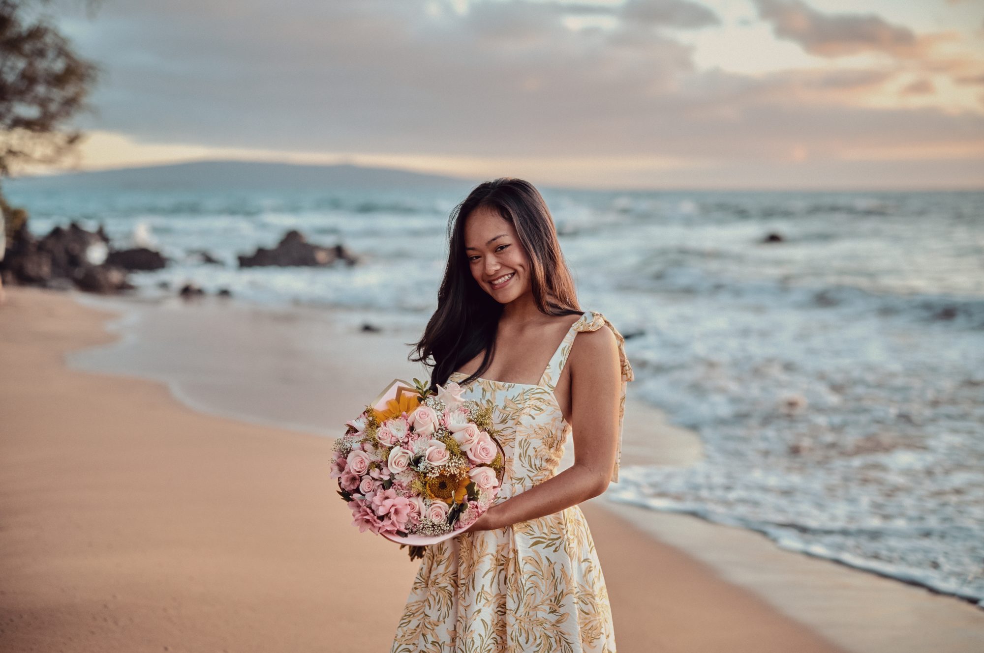 Mya Ige of Apuakea Weddings smiling on a Maui beach with a fresh bouquet