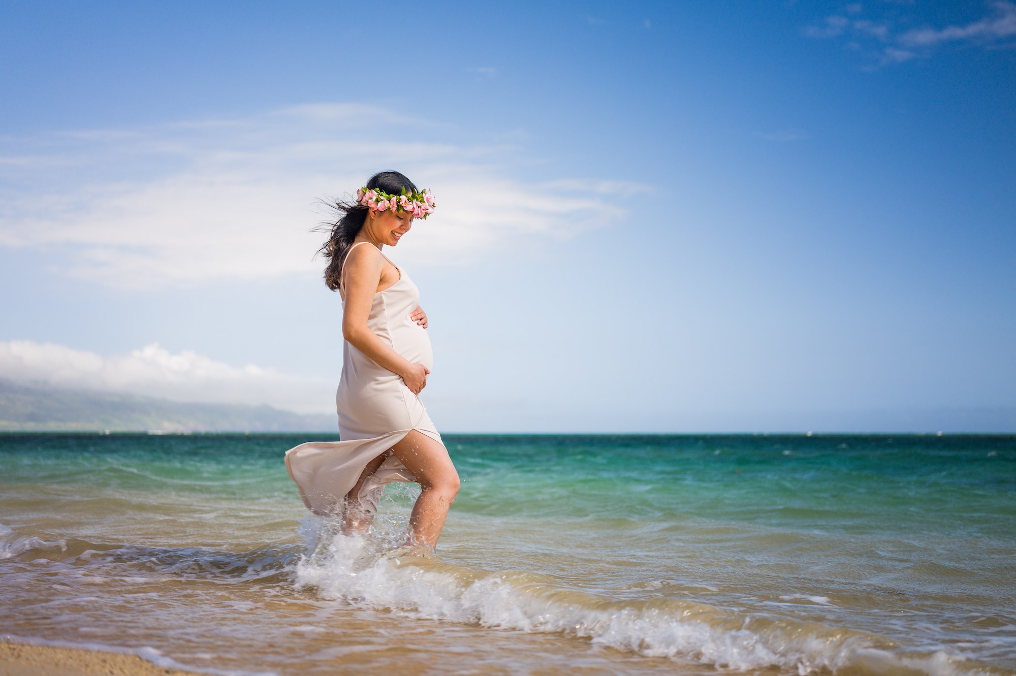 An expecting mother photographed beside turquoise water in Maui