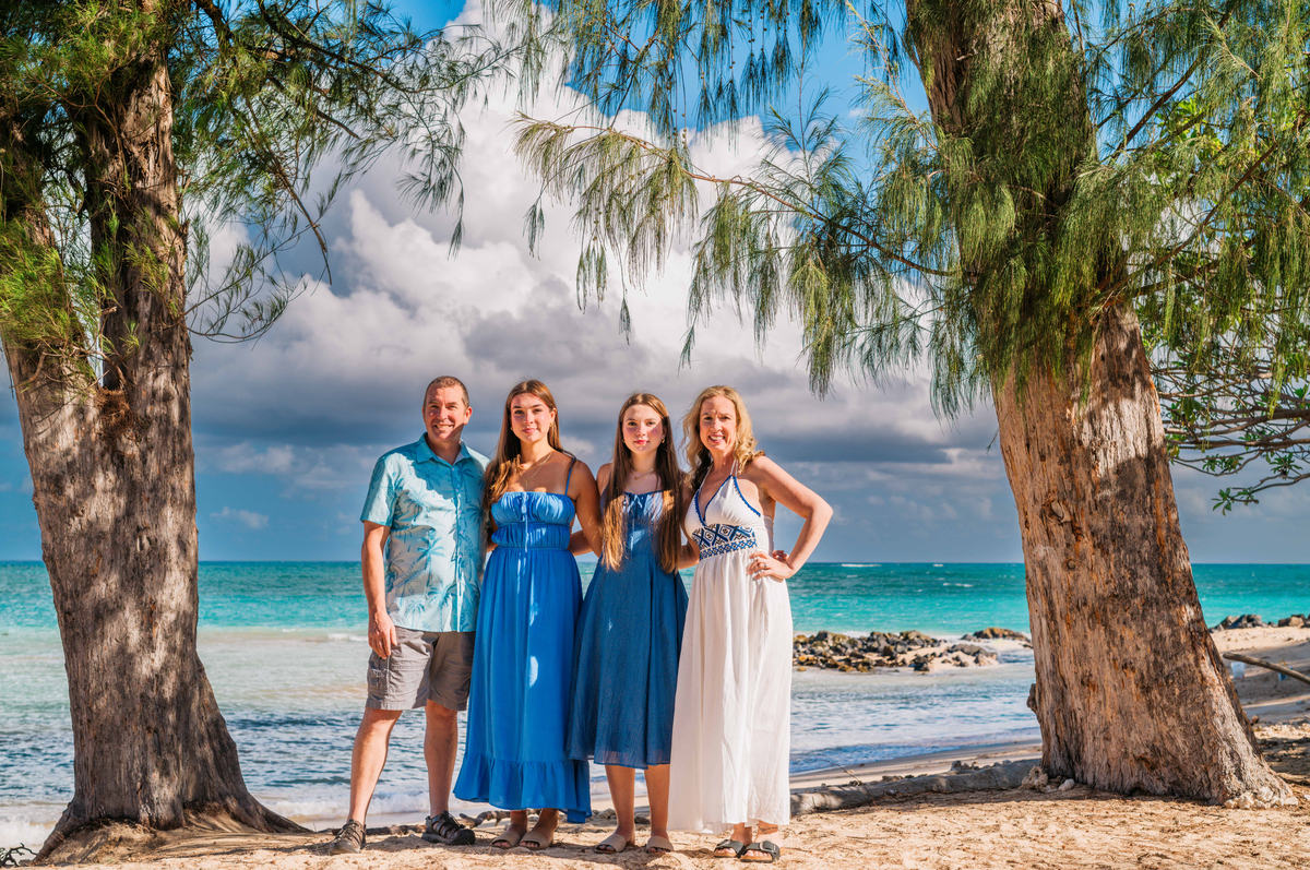 A family of four photographed beneath ironwood trees beside turquoise water on a Maui morning