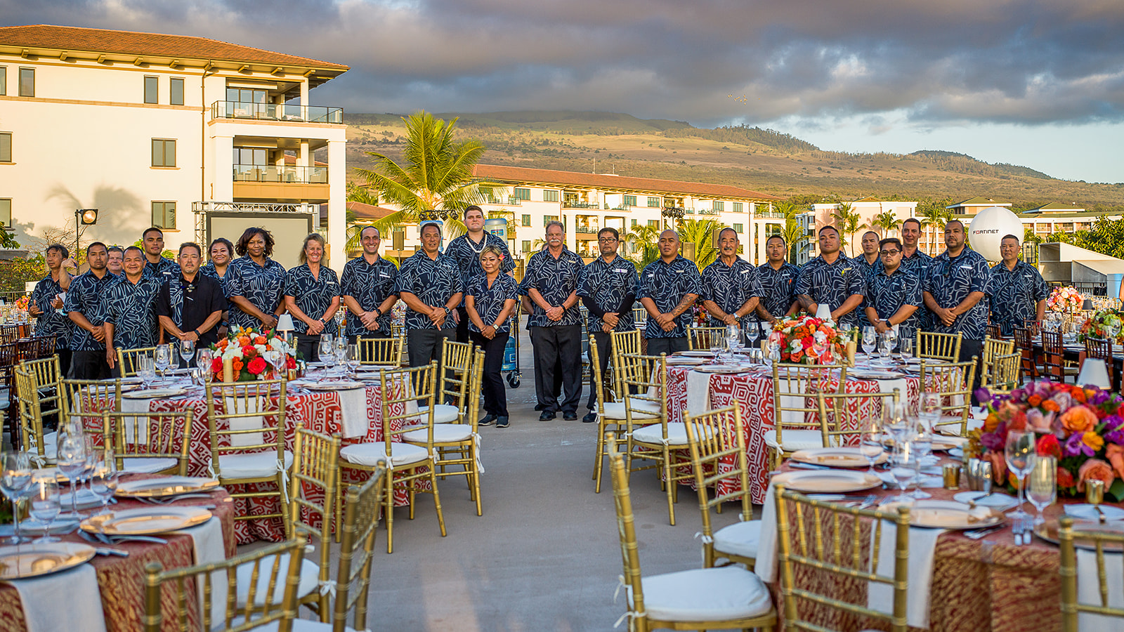 A large group photographed at an elegant outdoor corporate gala setup in Wailea
