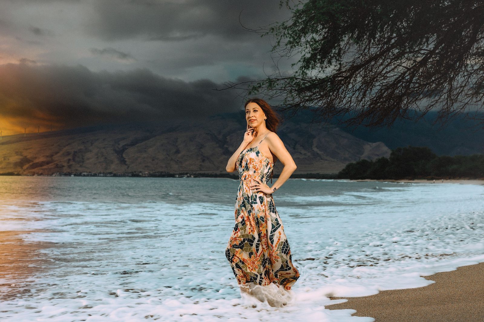 Una donna in un abito a stampa mosaico in posa sul bagnasciuga sotto nuvole tempestose al tramonto a Maui