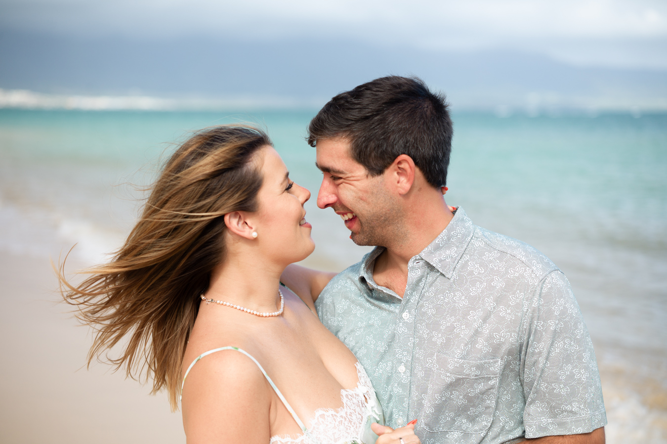 An engaged couple laughing together against turquoise Maui water during a Turquoise and Water Experience session