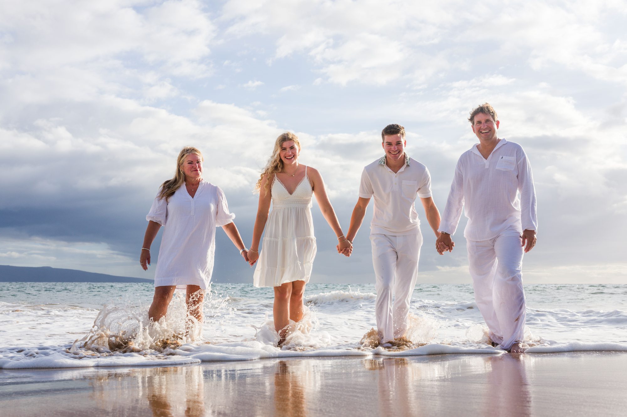 A family walking hand in hand through the surf in soft morning light in Wailea