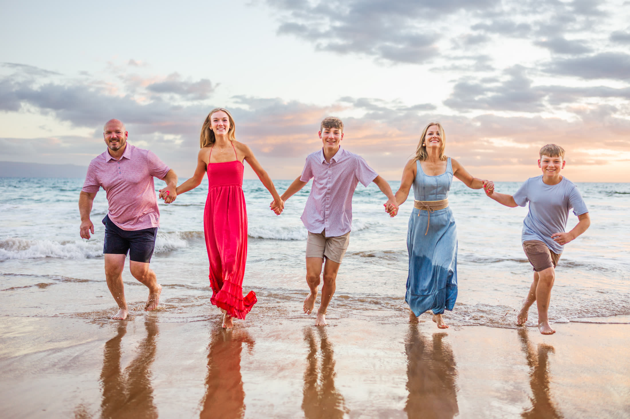 A family running hand in hand through the shoreline during a Maui sunset portrait session