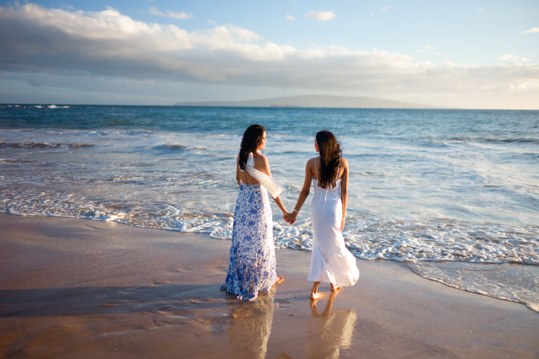 A mother and daughter walking hand in hand beside the ocean during golden hour in Wailea