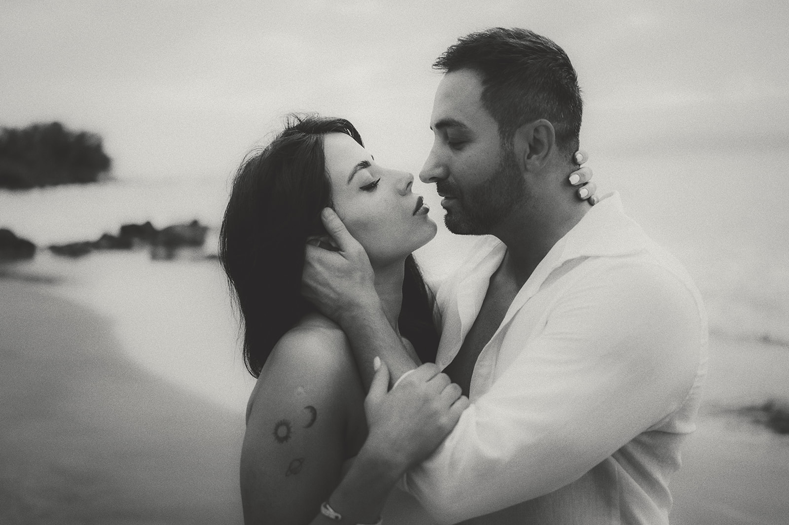 Couple moments before a kiss on a Maui beach, his hand at her cheek, in black and white