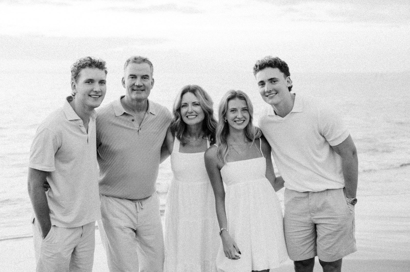 Smiling family of five arm in arm at the Maui shoreline, in black and white