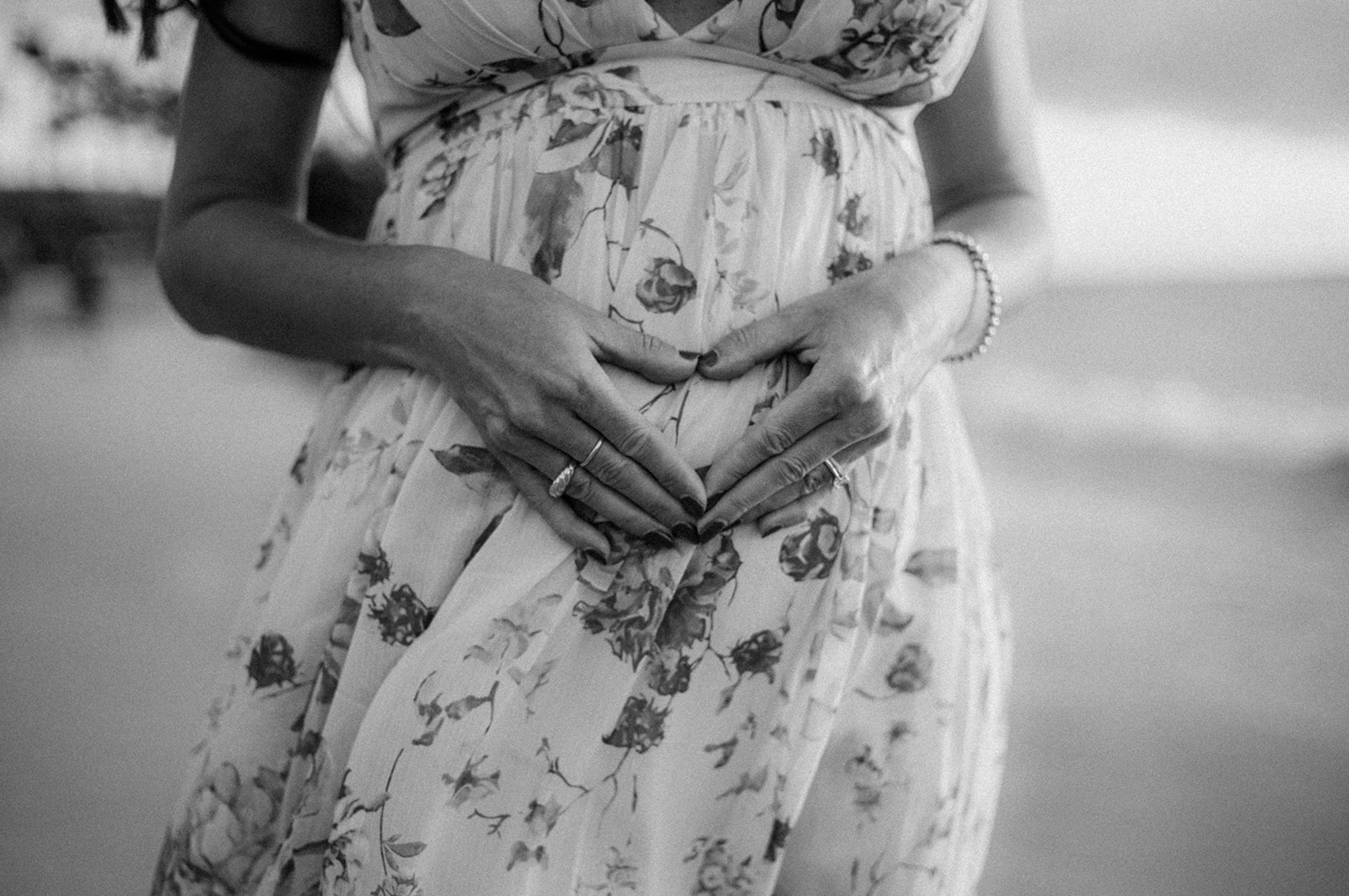 Expecting mother’s hands forming a heart over a floral maternity dress, in black and white