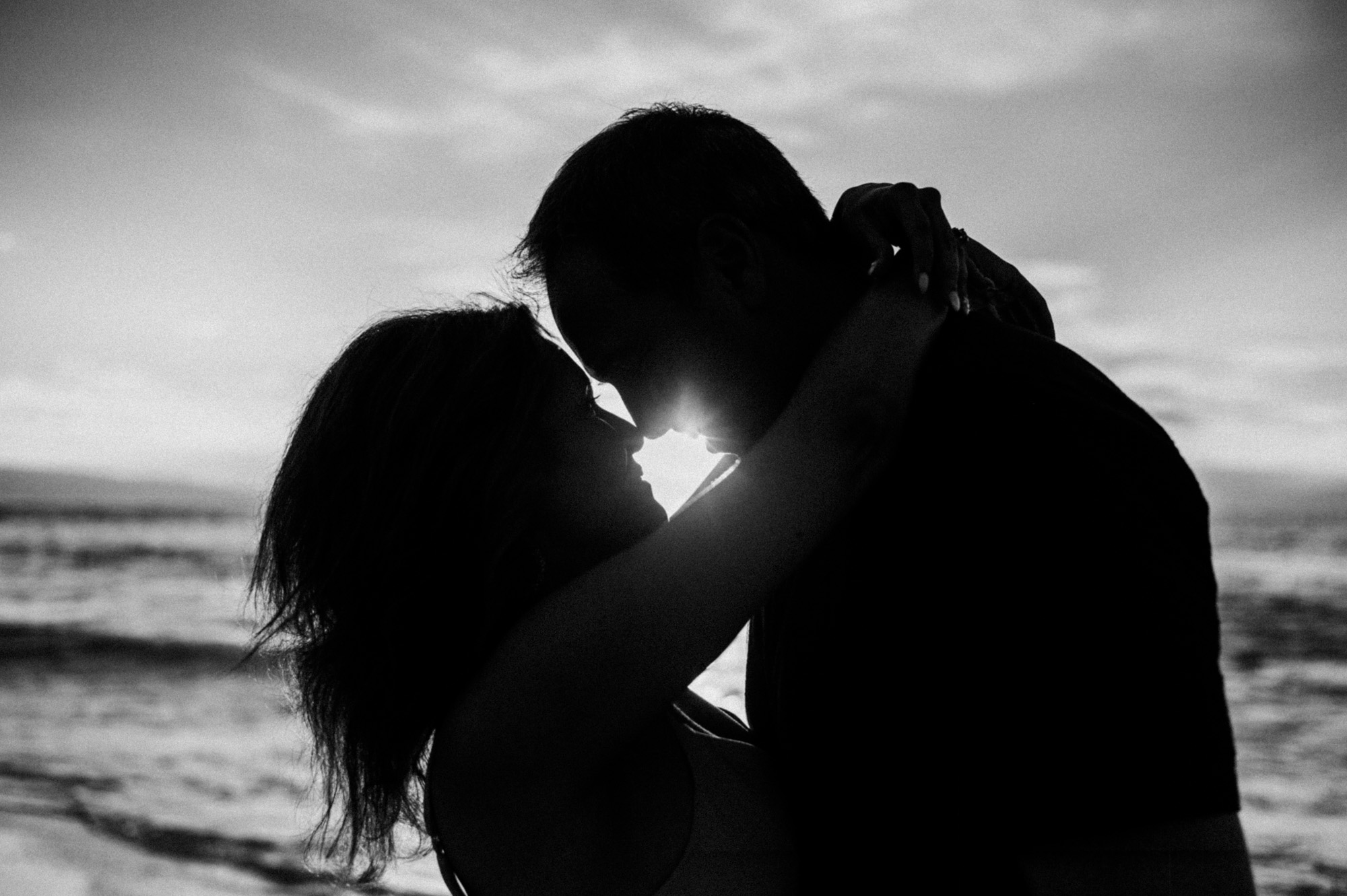 Black-and-white silhouette of a couple about to kiss, the sun glowing between them on a Maui beach