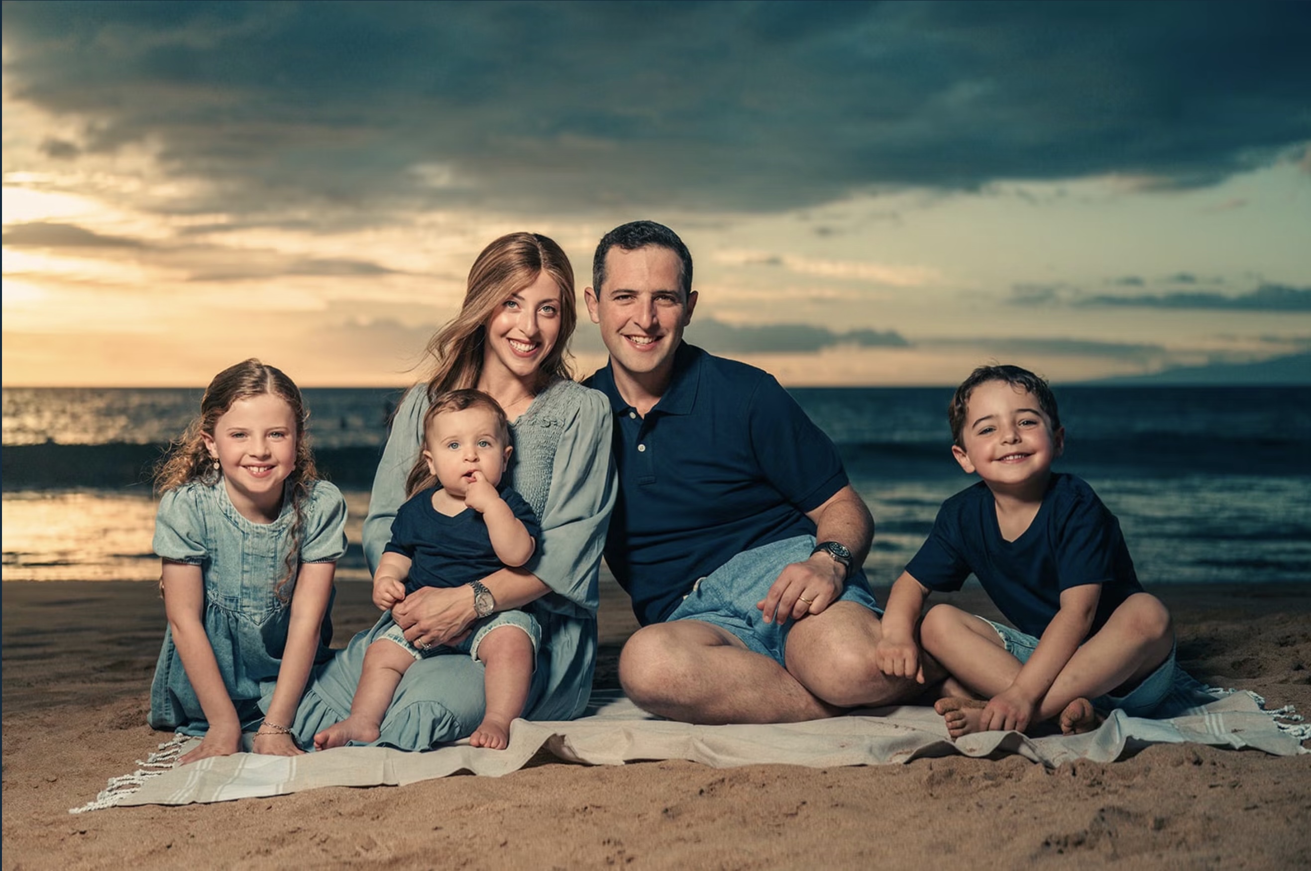 A family in rich blue clothing photographed against a golden Maui sunset