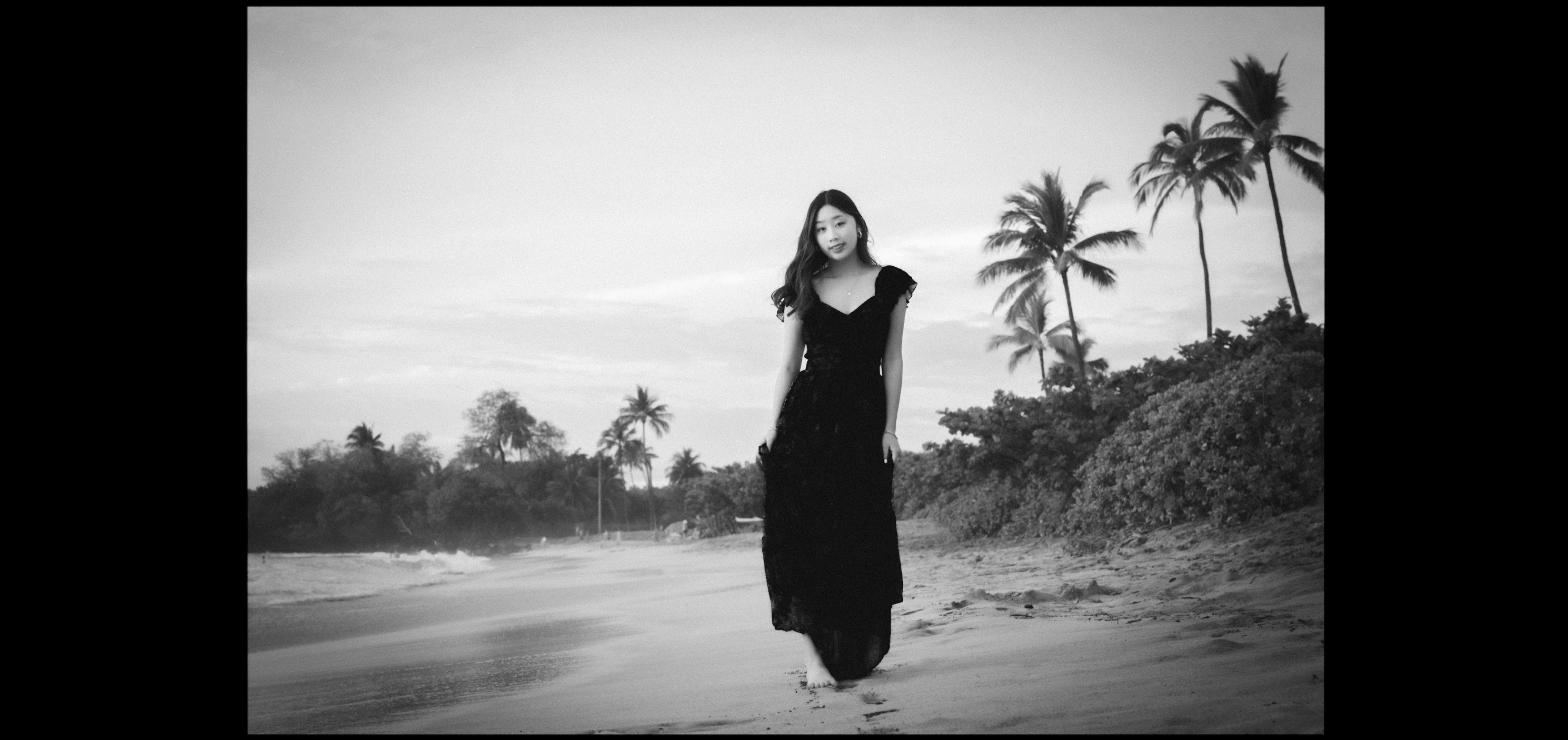 Woman in a black dress walking along a palm-lined Maui beach in black and white