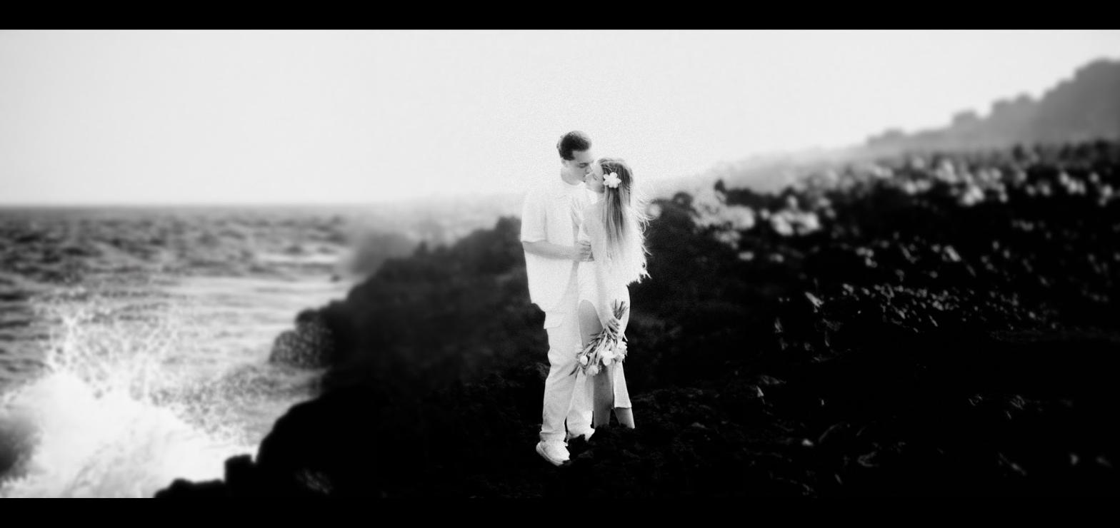 Couple kissing on a Maui cliffside surrounded by flowers in black and white