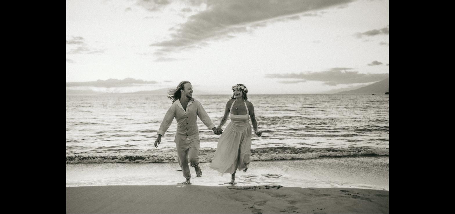 Couple laughing and running hand in hand along the shoreline in black and white