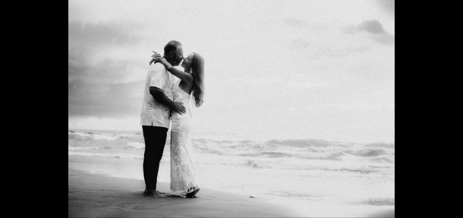 Couple sharing a kiss on a quiet Maui beach in soft black and white light