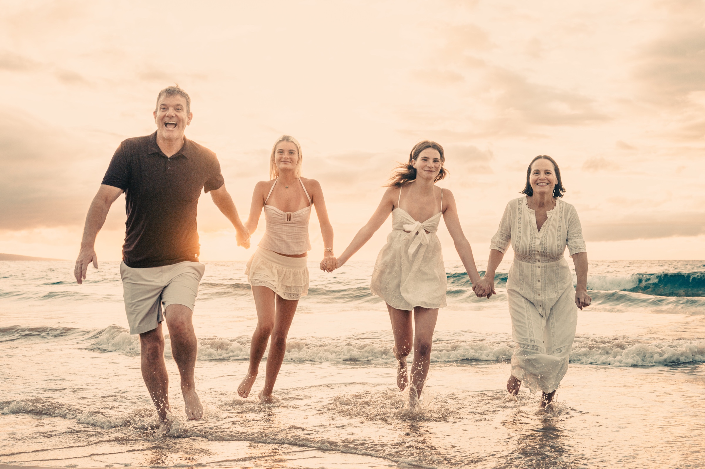 A family holding hands and running through the ocean at a golden Wailea sunset