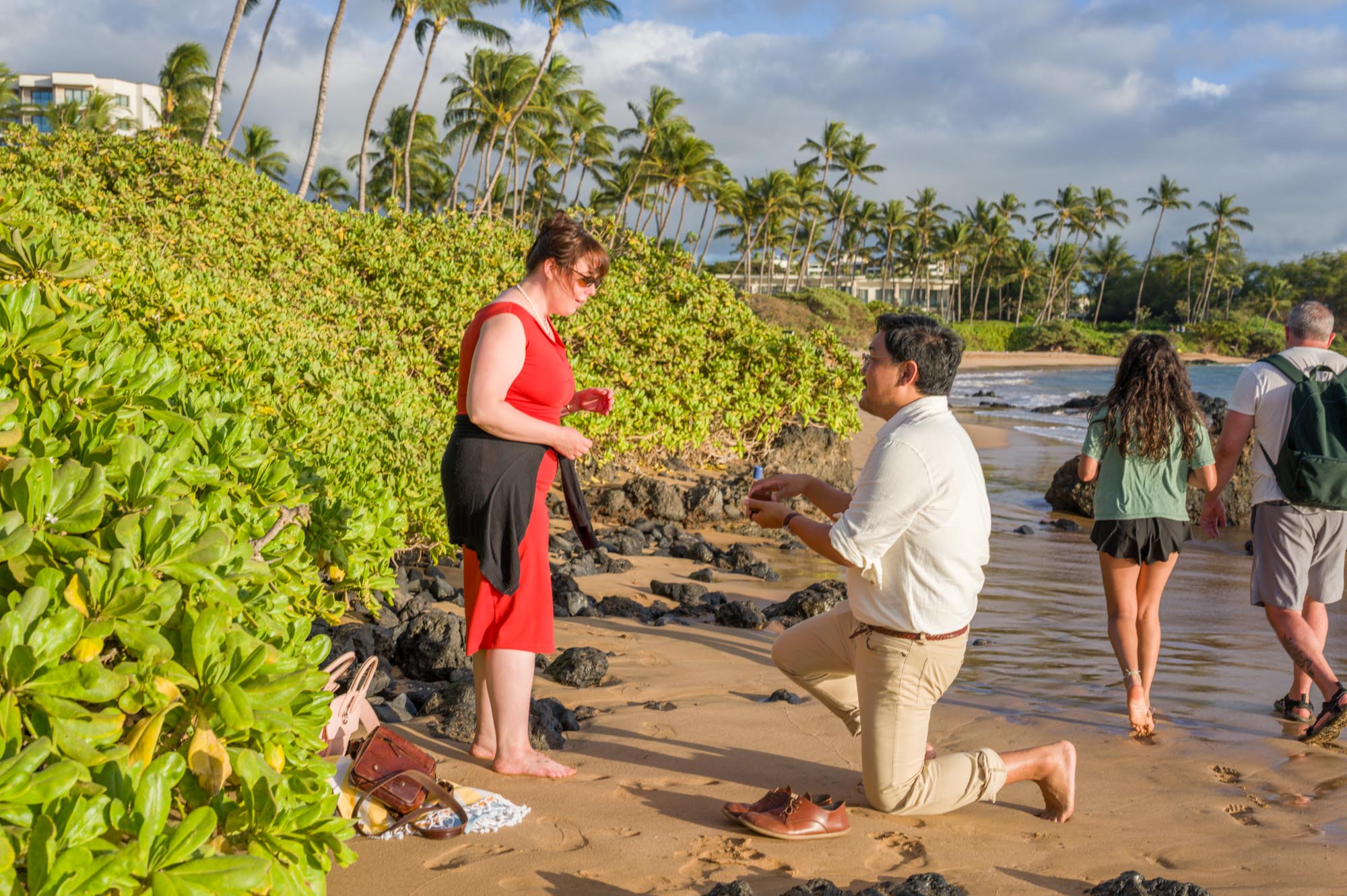 A surprise proposal on a public Maui beach as two visitors walk through the background