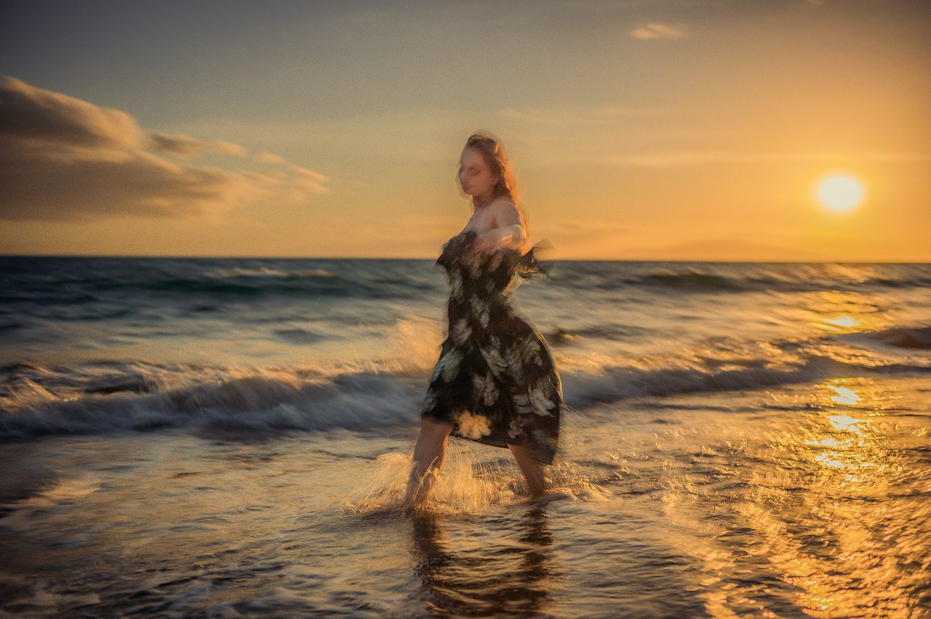 Mujer con vestido floral girando en la orilla mientras el sol se pone sobre Maui, desenfoque impresionista