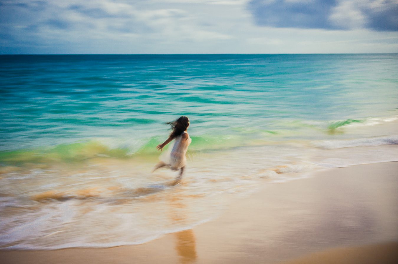 Una niña con vestido blanco corriendo por el oleaje turquesa de Maui, con un desenfoque de movimiento de estilo impresionista