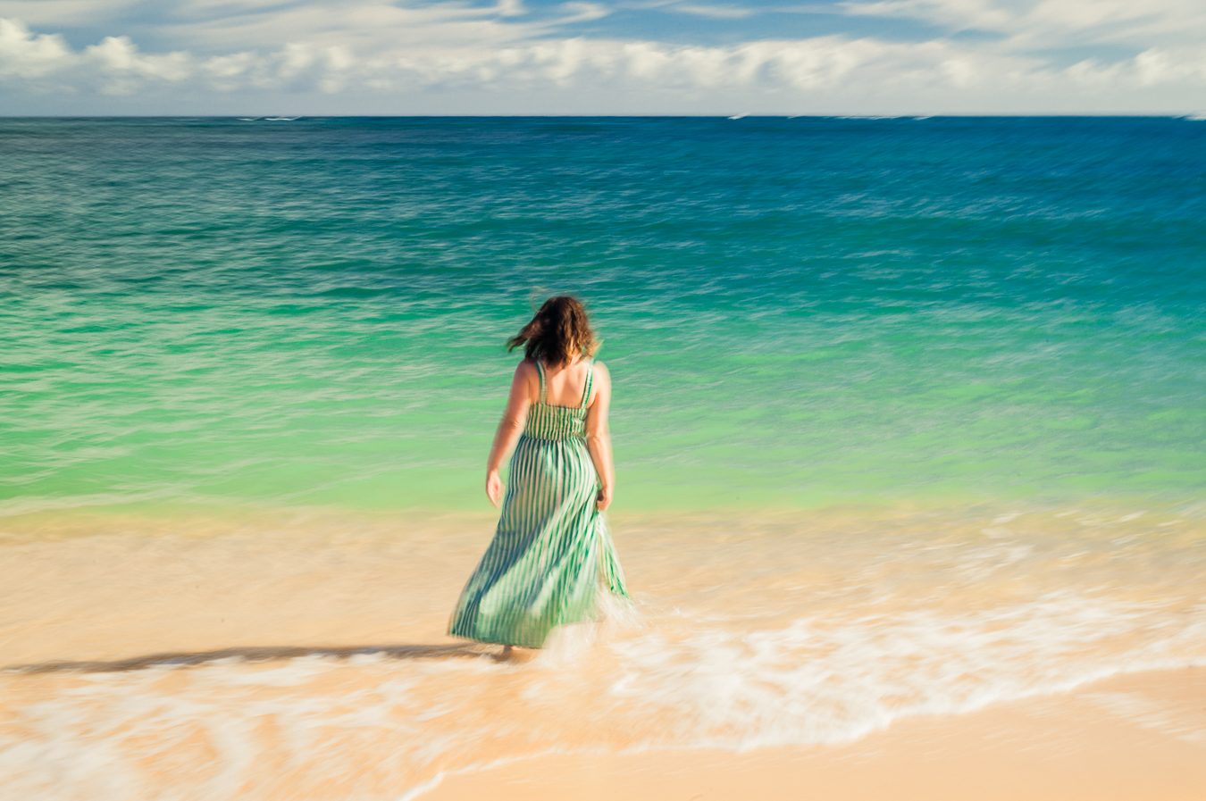Mujer con vestido a rayas verdes caminando hacia el oleaje turquesa de Maui, desenfoque de movimiento como una pintura