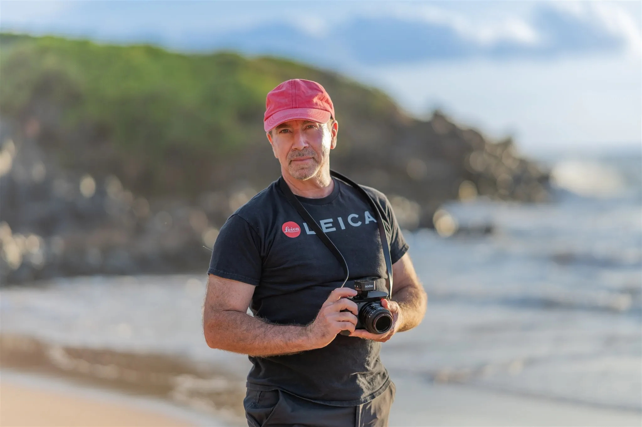 Laurence Balter, owner of Wailea Photo, holding a camera on a Maui beach