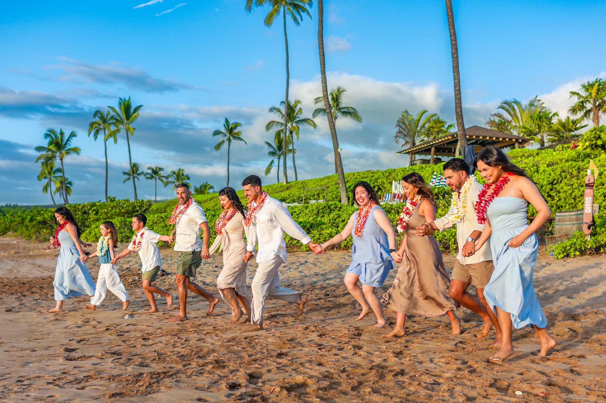 Eine große Familie mit Blumenketten geht Hand in Hand an einem Strand in Wailea entlang, während eines „Light and Bright“-Shootings