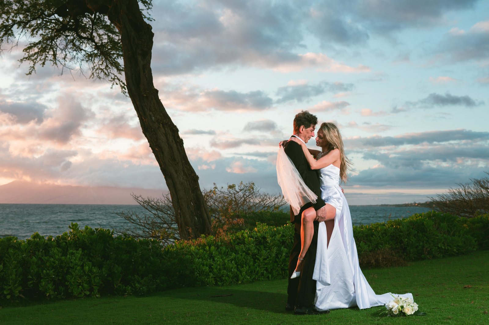A bride holding her bouquet and walking a stone garden path in Maui with mountains in the distance
