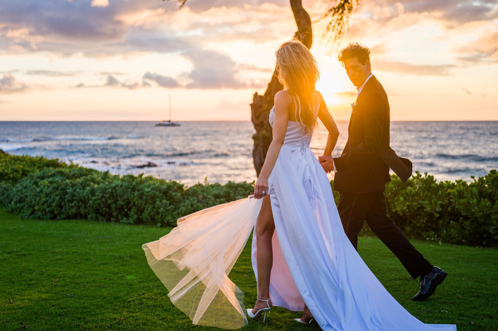 A bride and groom embracing beneath a tree at dusk with the ocean behind them in Maui