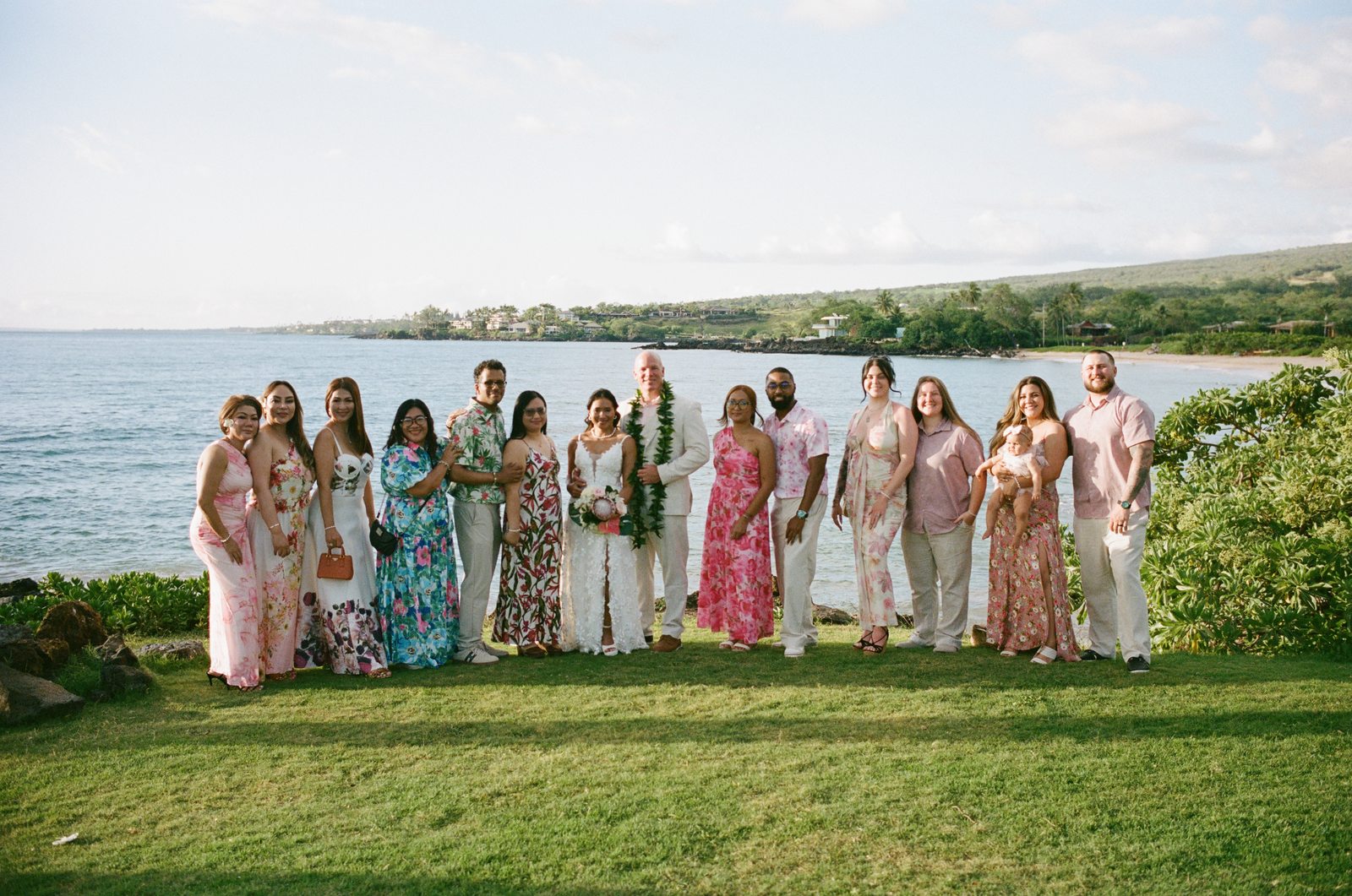 The bride, groom and their wedding party posed together on the grass above a Maui bay