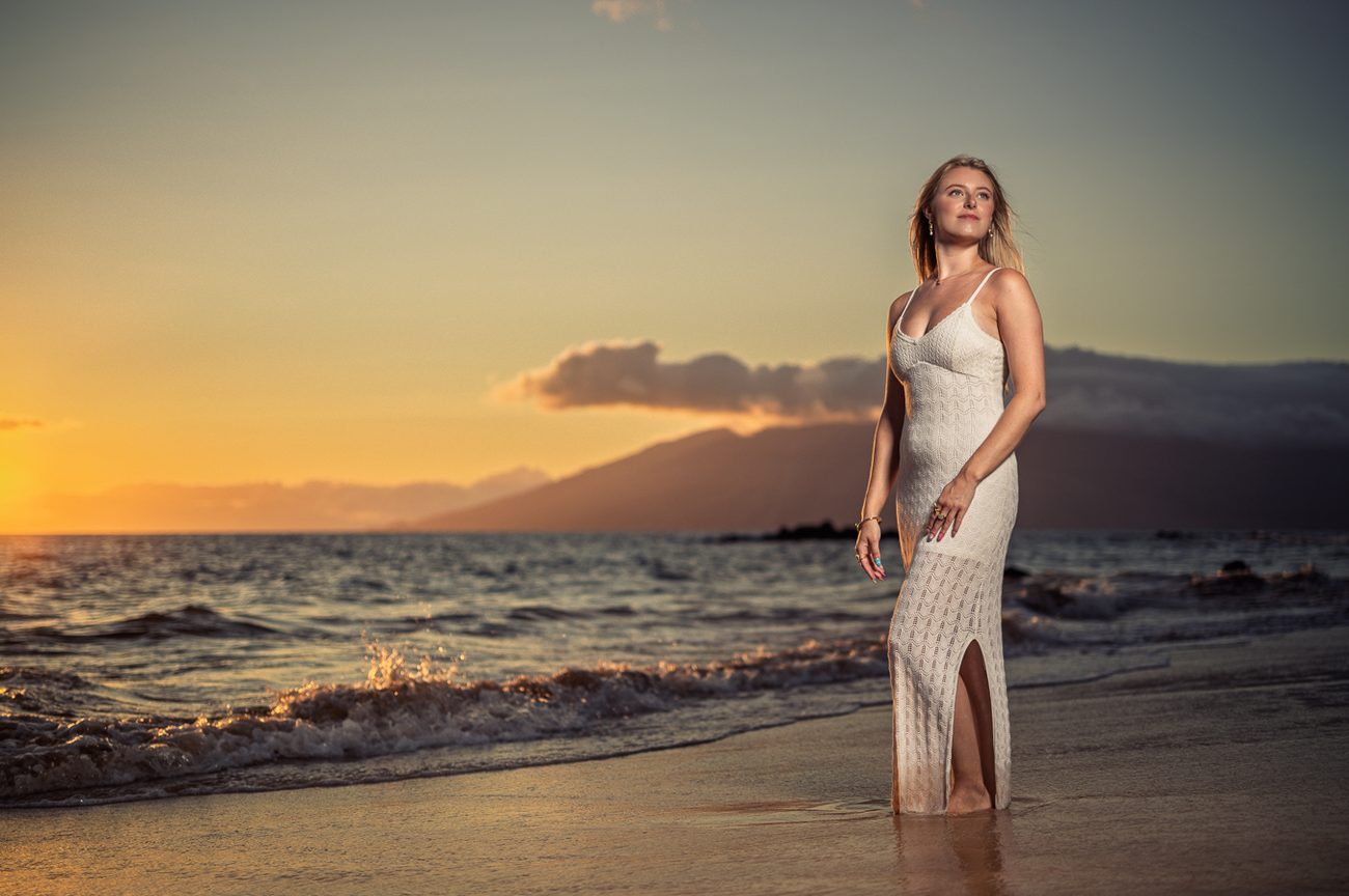 A senior in a cream knit gown in the shallows against a Maui sunset
