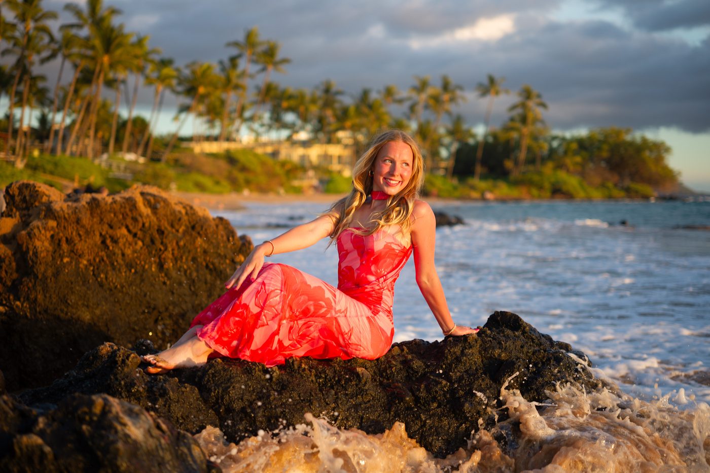 A senior seated on lava rock as surf breaks below, palms behind her in Maui