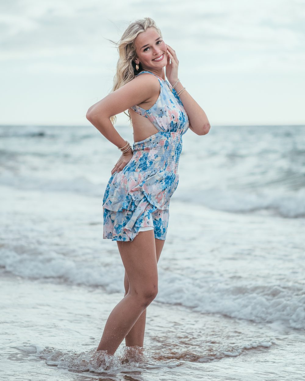 A senior standing in the shorebreak in a blue floral dress at Maluaka Beach