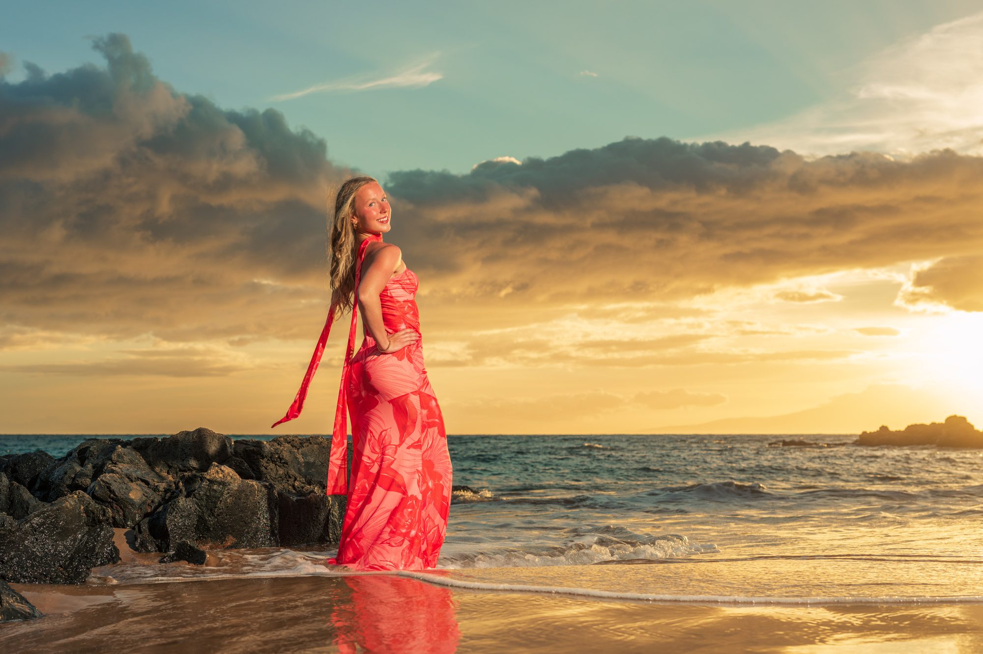 A high school senior in a coral dress at the water’s edge during a Maui sunset