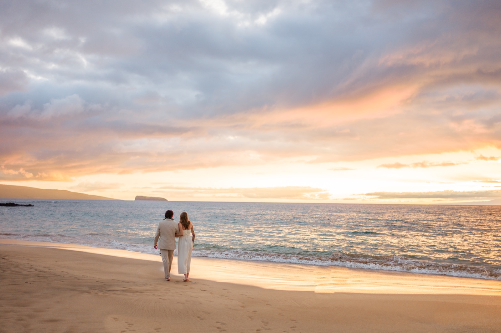 A newlywed couple walking together along a Maui beach at sunset