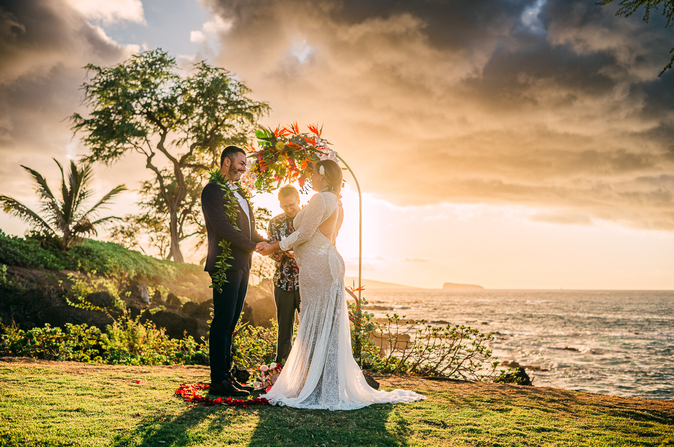 A wedding ceremony beneath a floral arch overlooking the ocean in Maui